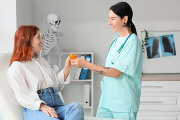 Fototapeta premium Tattooed female doctor giving pill bottle to patient in clinic