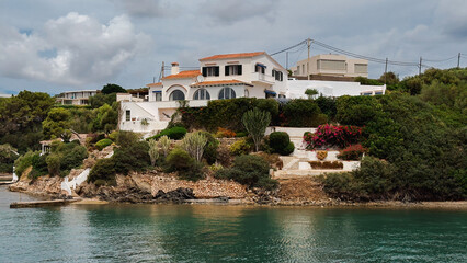 White villa with terracotta roof and arched windows on a green hillside overlooking calm turquoise...