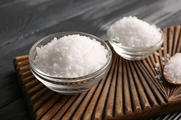 Board with bowls of sea salt on dark wooden background, closeup