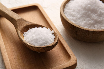 Wooden bowl of sea salt, spoon and board on light background, closeup