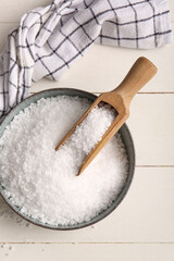 Bowl with sea salt and napkin on light wooden background