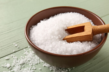 Bowl with sea salt and scoop on color wooden background