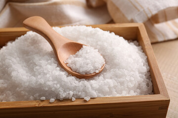 Wooden box with sea salt and spoon on table, closeup