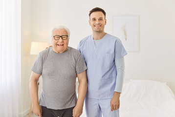 Obraz premium Portrait of happy health care worker with elderly man smiling and hugging in rehabilitation clinic. Young nurse with senior patient looking cheerful at camera. Nursing service and support concept.