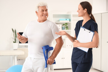 Fototapeta premium Female therapist and senior man with crutches in rehabilitation center
