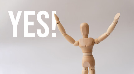 Close-up of a wooden mannequin with arms raised, expression of joy and the word 