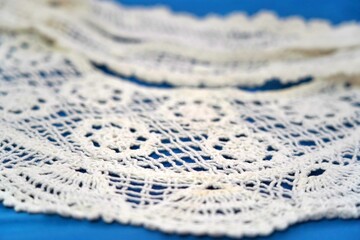 White crochet lace on blue fabric background with shallow depth of field