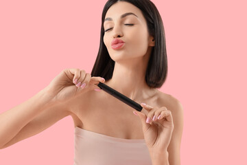 Beautiful young woman with mascara blowing kiss on pink background
