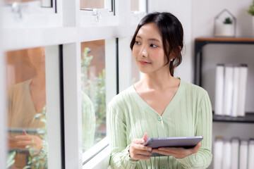 Portrait young asian business woman using tablet computer for relax and check social media online in living room at home office, businesswoman working on tablet for device wireless, business concept.