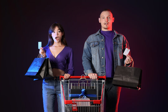 Surprised couple with shopping cart, credit cards and purchases on black background. Cyber Monday - Powered by Adobe