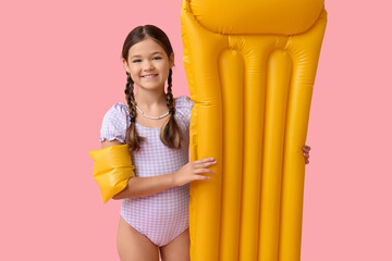 Obraz premium Cute little girl in swimsuit with inflatable armbands and mattress on pink background