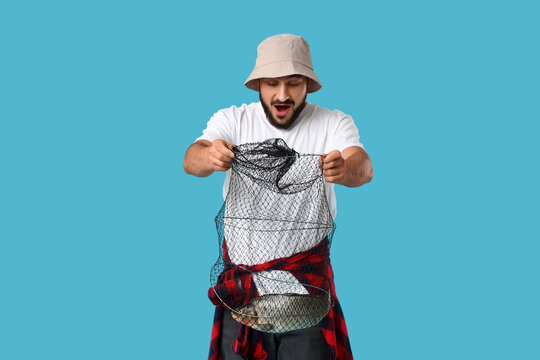 Surprised young man with caught fish in keepnet on blue background