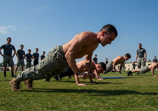 Group of shirtless soldiers in camouflage pants doing push-ups during an intense outdoor military fitness training session