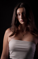 Fototapeta premium Fashion model posing in studio with serious expression, wearing white top and gold necklace on black background