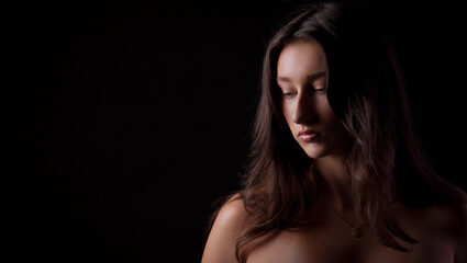 Fashion model posing in studio with black background, looking down with serious expression