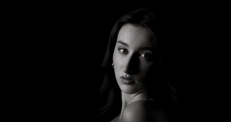 Fototapeta premium Black and white portrait of beautiful model posing in studio with bare shoulders and dark background, creating a dramatic and evocative image