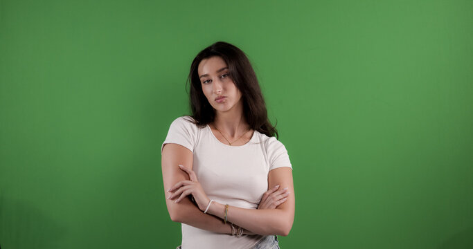 Young woman posing with crossed arms on green screen background, expressing disagreement and disapproval