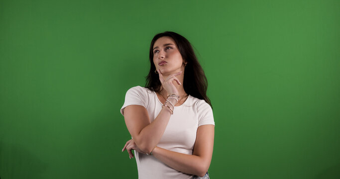 Young woman posing as a model, thinking with hand on chin, during a studio photoshoot against a green screen backdrop