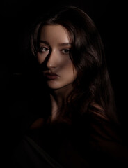Naklejka premium Fashion studio portrait of a beautiful young female model posing in shadows with contrasting light on her face