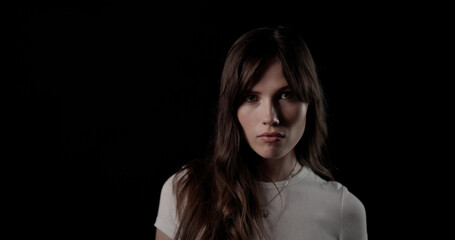 Studio portrait of confident model posing with serious expression, wearing white t shirt on black background