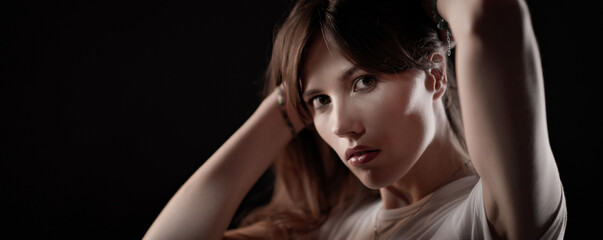 Young woman model adjusting her hair with hands during studio photoshoot against black background