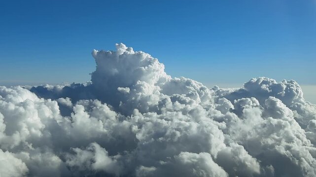 An immersive pilot&rsquo;s eye perspecvtive taken from the cockpit of a jet airplane flying above a cottony storm clouds under a deep blue sky, with a threatening cumulonimbus storm cloud ahead.