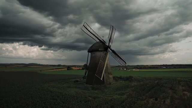 Old Windmill on Green Field Under Dramatic Stormy Sky in Rural Landscape