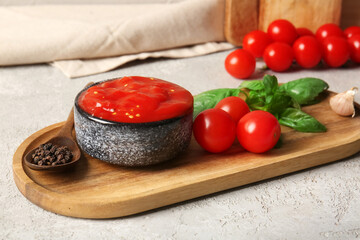 Bowl of tasty tomato sauce with basil leaves and peppercorns on grey background