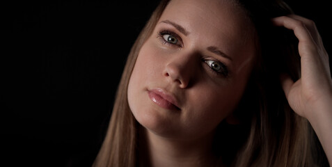 Fototapeta premium Young woman with light eyes and long hair posing in studio, touching her hair with her hand