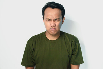 Obraz premium Angry and mad face of Asian man in dark green shirt on isolated white background