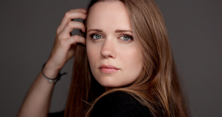 Professional model posing and adjusting her hair in a studio photoshoot, showcasing her beauty and...