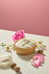 Close display of shea butter pieces beside roses and chamomile flowers on neutral surface. Natural cosmetic ingredient photography for branding visuals.