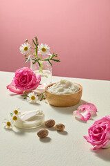 Arrangement of raw shea butter with fresh roses and chamomile blossoms in light background. Organic skincare theme with minimalist product placement idea.