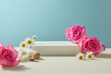 Front view of shea butter chunks, roses and chamomile arranged across neutral blue background....