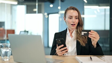 Executive manager, leader of company businesswoman sits in a modern office. She uses a smartphone and credit card for an online purchase, becoming excited and happy with the successful transaction. - Powered by Adobe