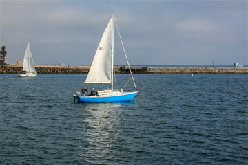Blue Sailboat on the Water Near Jetty with People on Board