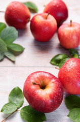 Fresh red gala apples with green leaves and water drops on rustic wooden surface