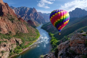 Obraz premium Colorful hot air balloon soaring over a river and mountains in a bright landscape