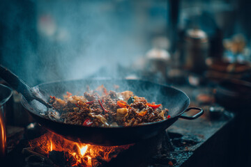Close-up of sizzling meat being stir-fried in a wok with flames and steam rising in a rustic kitchen. Authentic Asian cooking scene with rich colors, heat, and motion