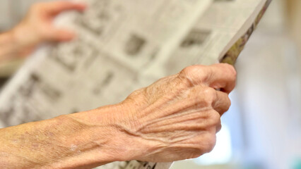 室内で新聞を持って広げる高齢者の手元_右向き
