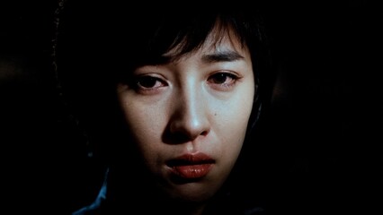 A person's face partially obscured by shadow, with a single tear. Regret, guilt, criminal, consequences, legal.