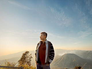 A guy posing with Mount Bromo and Mount Batok at the background, with beautiful and colorful sunrise sky in the early morning. In Bromo Tengger Semeru National Park, Indonesia. Travel photography