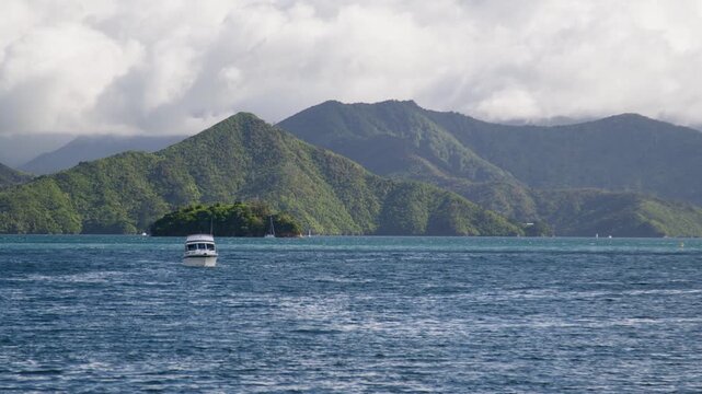 A boat slowly floating towards the camera through the Marlborough Sounds in the South Island of New Zealand with Mabel island in the background.