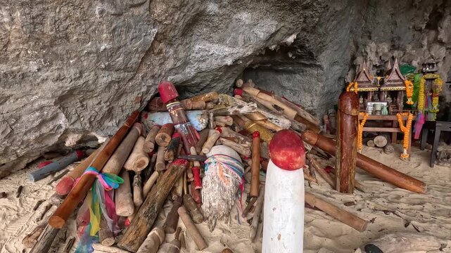 Walking handheld POV towards a Hindu animist shrine decorated with offerings and phallic symbol called lingams in Phra Nang Cave or Princess Cave, authentic local thai folklore. Krabi, Thailand