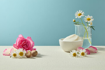 Soft horizontal composition with shea butter, roses in vase and chamomile. Clean natural beauty ingredient display for skincare advertising concepts.