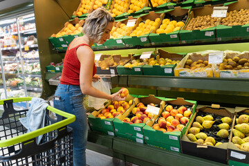 Woman buying fresh peaches in supermarket produce section