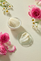 Vertical still life photo with shea butter placed beside rose flowers and chamomile. Minimalist setup for beauty ingredient photography with space for product text.