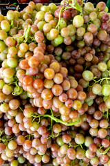 Close-up of juicy, ripe grapes with shades of red, pink, and green tightly clustered on stems, capturing peak freshness and natural shine in open-air market setting