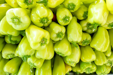 Close-up of vibrant pale green bell peppers with shiny skin and fresh stems, arranged in a dense pile, showcasing peak ripeness and local harvest