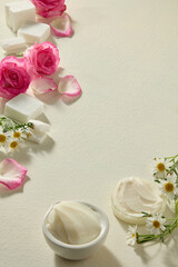 Top view composition of shea butter pieces, roses and chamomile blossoms scattered on cream background. Flat lay still life ideal for natural cosmetic product visuals.